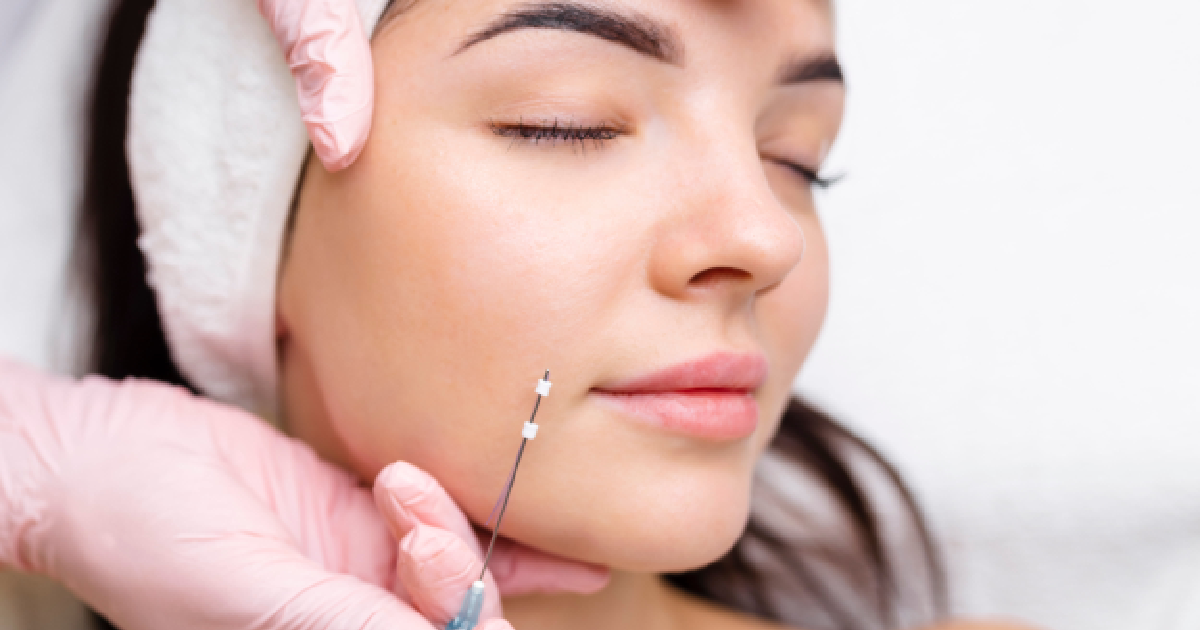 Young woman with eyes closed receiving a PDO thread lift procedure on her cheek by a professional wearing pink gloves in a clinical setting in Lexington, KY