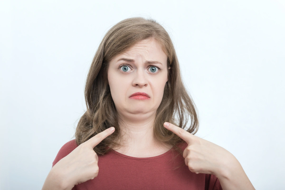 Woman pointing to her double chin before non-surgical treatment for submental fat reduction with Kybella or CoolSculpting Elite.